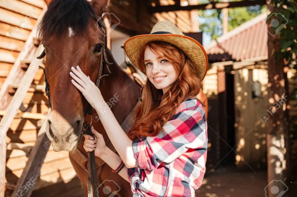 63565663-happy-redhead-young-woman-cowgirl-with-her-horse-in-village